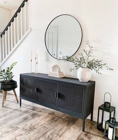 a living room with a black cabinet and mirror on the wall next to potted plants