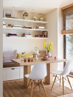 a dining room table with two chairs next to it and shelves on the wall above