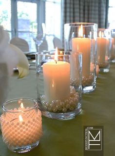 candles are lined up on a table with glass vases filled with beads and pearls