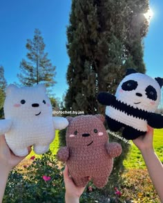 three handmade stuffed animals are held up in the air with trees and grass behind them