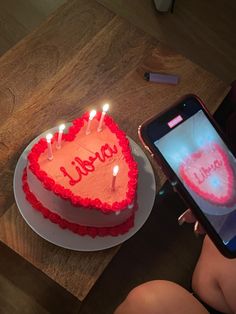 a heart - shaped cake with candles is being held up by a person using a cell phone