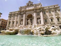 a fountain in front of a large building with statues on the top and water running down it