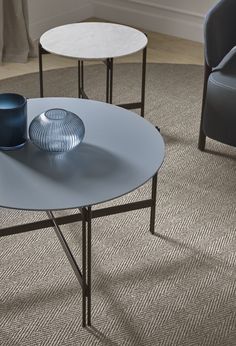 two glass tables sitting on top of a carpeted floor next to blue vases