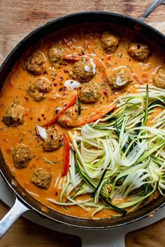 a skillet filled with meatballs and veggies on top of a wooden table