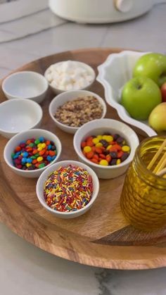 an assortment of confections are arranged in bowls on a wooden tray next to apples