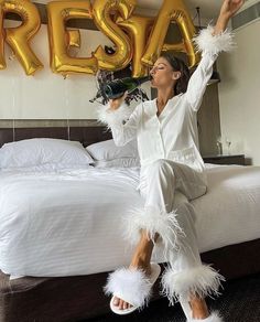 a woman sitting on top of a bed with her arms in the air and wearing white feathers