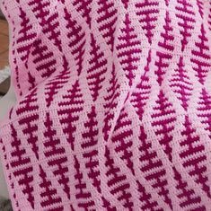 a pink and white crocheted blanket sitting on top of a bed