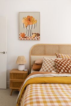 a bed with orange and white checkered sheets in a bedroom next to a painting on the wall