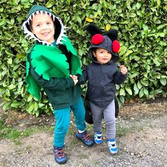 two children dressed up in costumes standing next to each other on the ground with bushes behind them