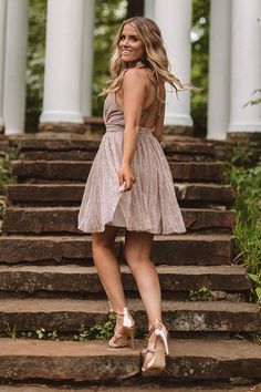 a woman standing on steps in front of a building with columns and trees behind her