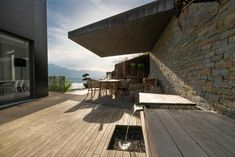 a wooden deck with tables and chairs next to a stone wall on the side of a building