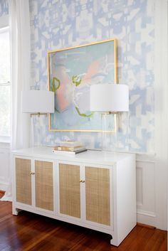 a white sideboard with two lamps on it in front of a blue and white wallpaper