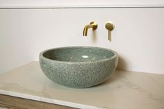 a bowl shaped sink on top of a counter next to a faucet and gold fixtures