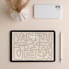 the tablet is next to a phone, pen and plant on the table with it's cover