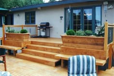 a wooden deck with planters and steps leading up to the front door, next to an outdoor grill