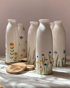 five vases with flowers painted on them sitting on a white table cloth next to slices of wood