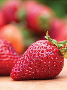 two strawberries sitting on top of a wooden table next to other fruit in the background