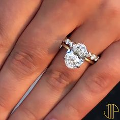 a woman's engagement ring with two pear shaped diamonds on her finger and an oval diamond in the middle