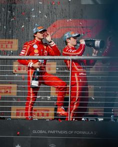 two men in red racing suits standing next to each other and confetti falling from the sky