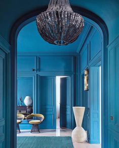 a blue hallway with a chandelier hanging from it's ceiling and an arch leading to another room