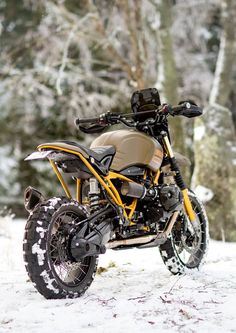 a yellow and black motorcycle parked in the snow next to some tree's on a snowy day