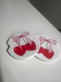 two plates with cherries on them are sitting on a counter top, one has a pink bow and the other is red