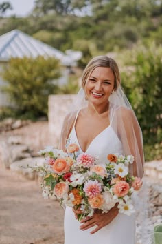 a woman in a white dress holding a bouquet of flowers and smiling at the camera