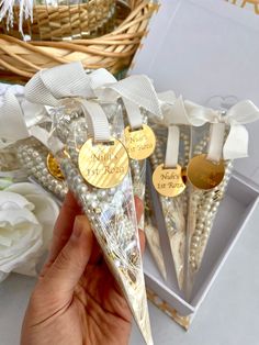 someone is holding three wedding favors in front of some flowers and a basket with white roses