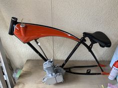 an orange and black motor bike sitting on top of a wooden table next to a wall