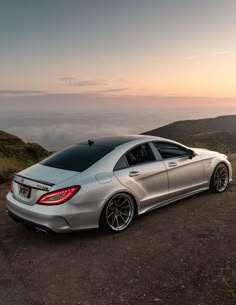 a silver car parked on the side of a mountain at sunset with fog in the background