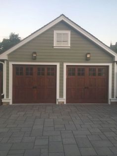 two brown garage doors are on the side of a gray and white house with brick driveway