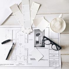 the table is covered with architectural drawings, pens and paper on top of it next to a cup of coffee