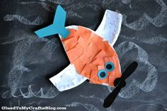 an orange fish made out of construction paper on a black surface with blue eyes and nose