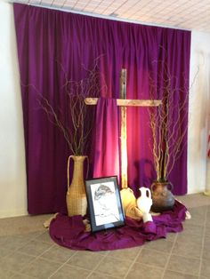 purple drapes and vases on the floor in front of a cross with branches