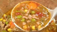 a white spoon filled with soup on top of a wooden table