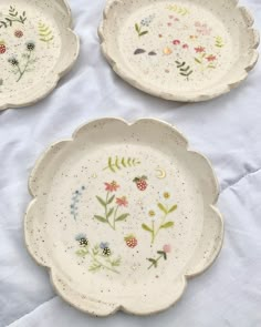 three plates with flowers painted on them sitting on a white cloth covered tablecloths