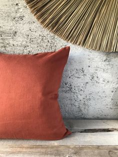 an orange pillow sitting on top of a wooden bench next to a wicker lamp