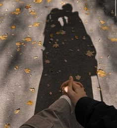 two people holding hands in front of a shadow of a person on the ground with leaves all over them