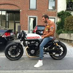 a man sitting on top of a motorcycle parked in front of a building next to a car