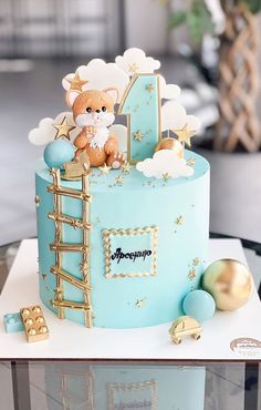 a blue cake with gold decorations and a teddy bear sitting on top of the number one