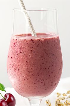 a smoothie in a glass with a straw sticking out of the top and cherries on the side