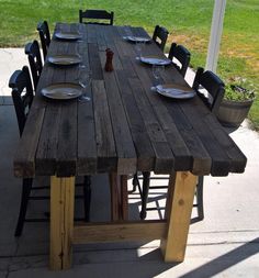 a wooden table with plates and wine glasses on it in front of a grassy area