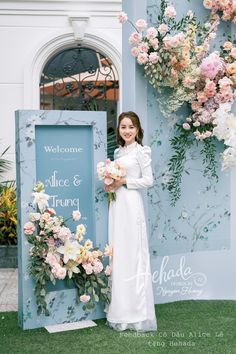 a woman standing in front of a sign with flowers on it and holding a bouquet