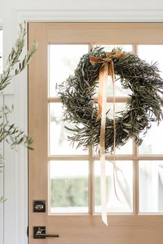 a wreath hanging on the front door of a house with a ribbon tied around it