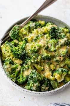 a bowl filled with broccoli and cheese on top of a white tablecloth