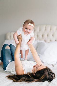 a woman laying on top of a white bed holding a baby in her arms and smiling at the camera