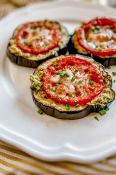 three stuffed eggplant halves topped with tomatoes and green onions on a white plate