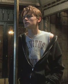 a young man standing next to a metal pole in front of a building and looking off into the distance