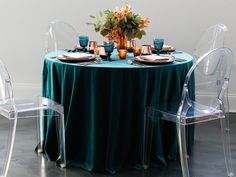 the table is set with clear plastic chairs and blue linens for an elegant dinner