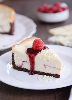 a piece of cheesecake with raspberries on top and another slice in the background